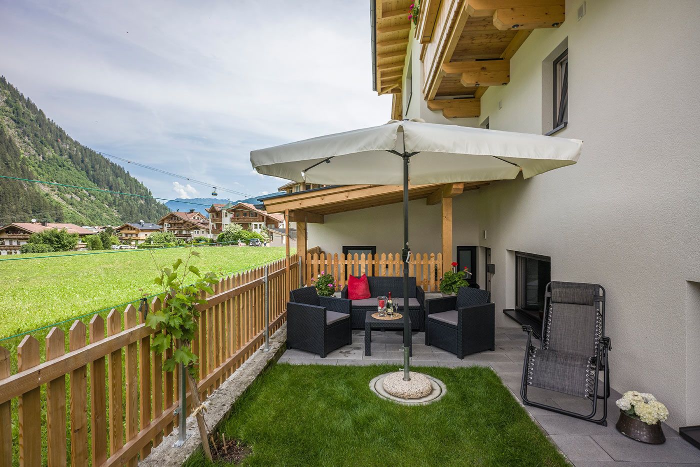 A photo of a garden with a large umbrella and chairs underneath