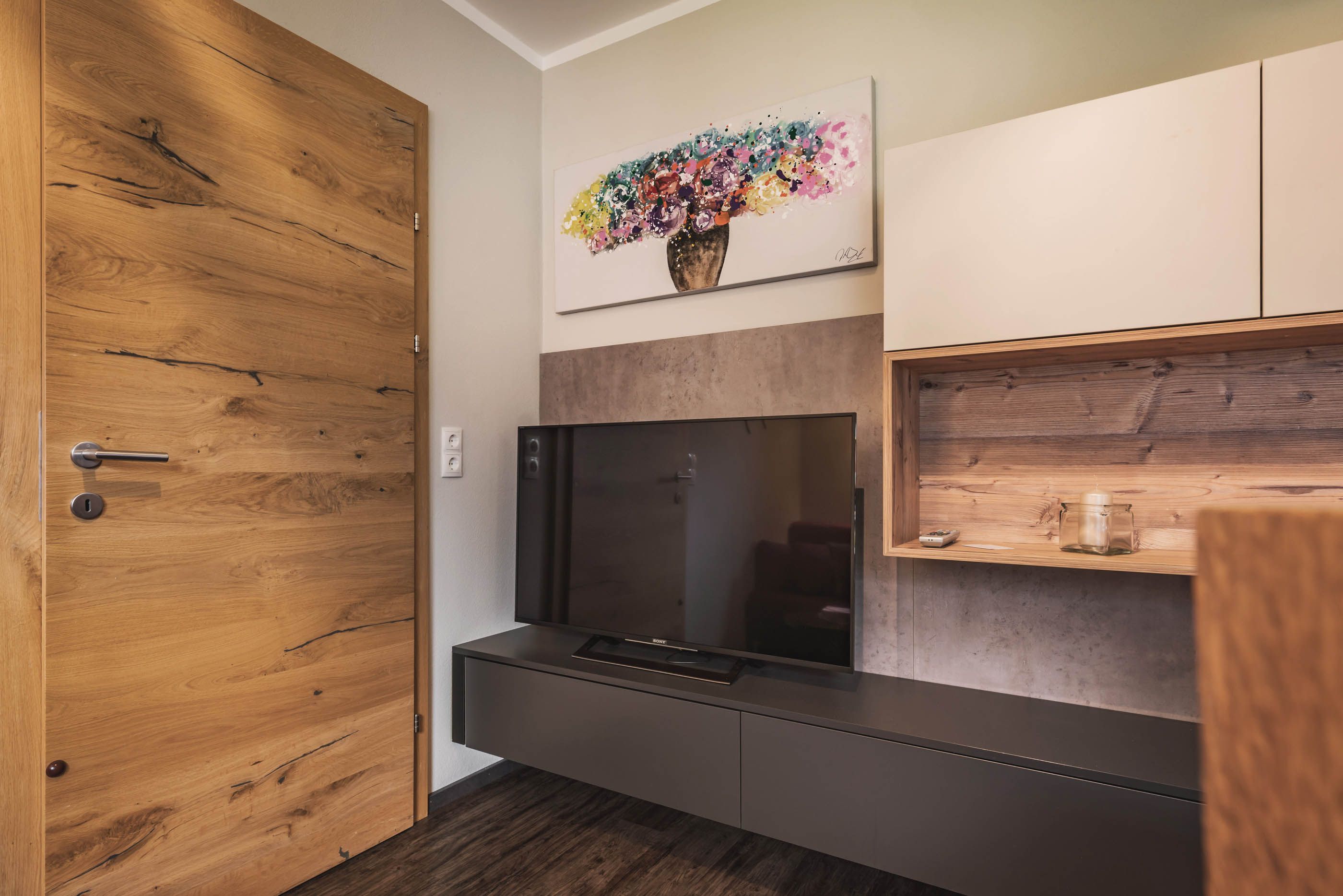 Moderner Fernseher im Wohnbereich mit Holzschränken und buntem Wandbild