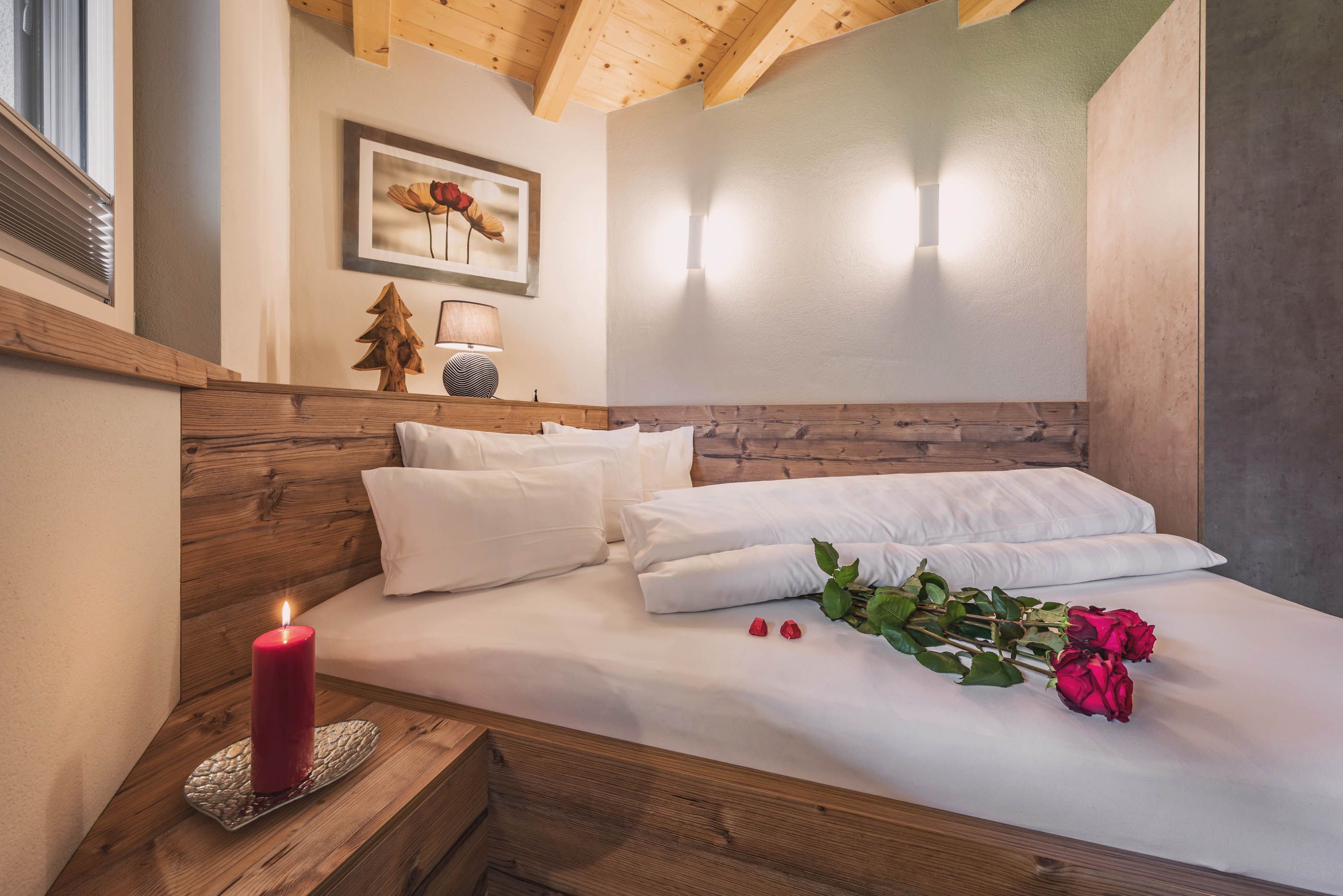 A romantic bedroom with wood paneling, double bed, candle and red roses as decoration