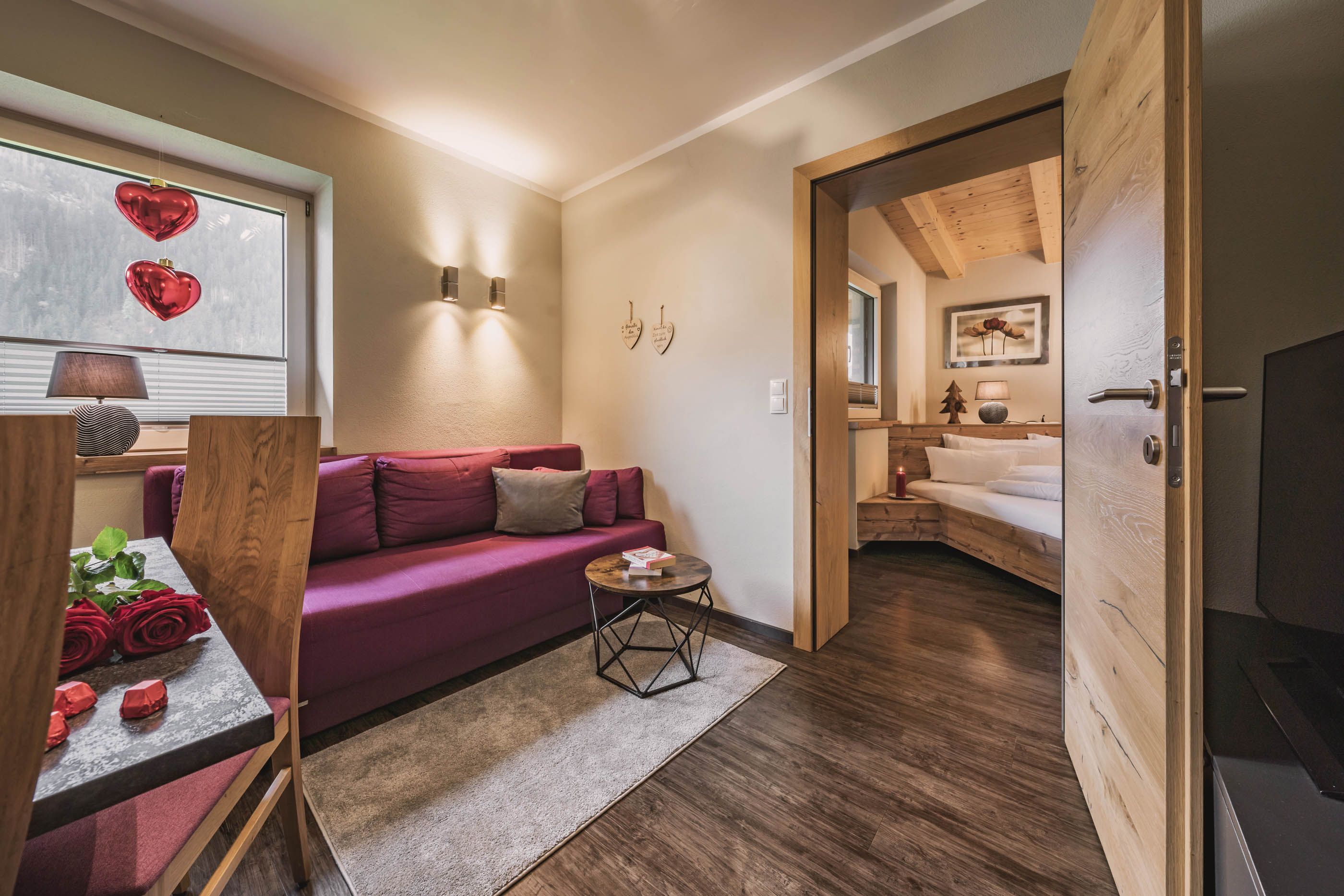 Gemütlicher Wohnbereich mit rotem Sofa, Couchtisch und Blick ins Schlafzimmer